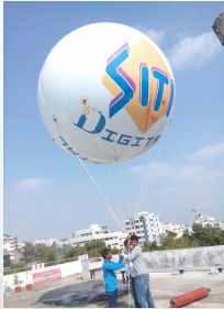 White inflatable balloon with logo floating in sky and person holding string