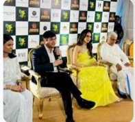 Four people sitting on chairs at an event with Sri Krishna Jewellery branding behind